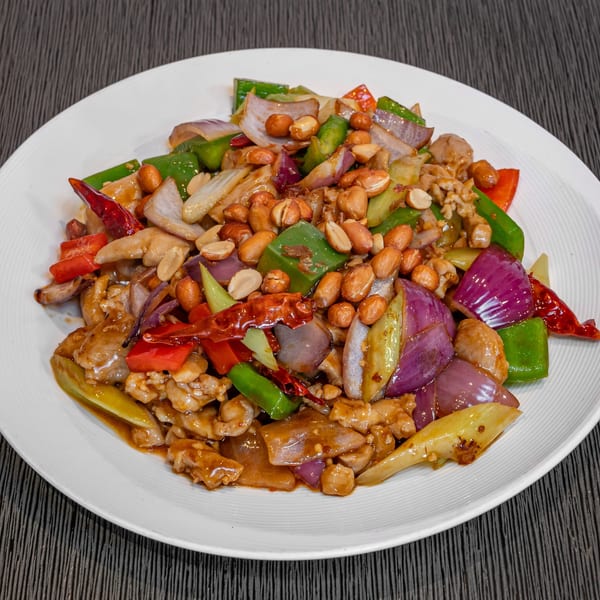 Kung Pao chicken with peanuts, red and green peppers, and onions on a white plate.