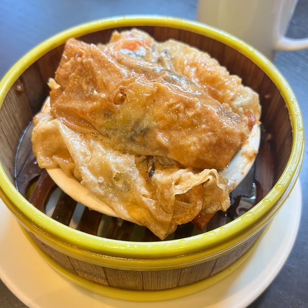 Steamed bean curd skin rolls with filling, served in a bamboo dim sum basket.