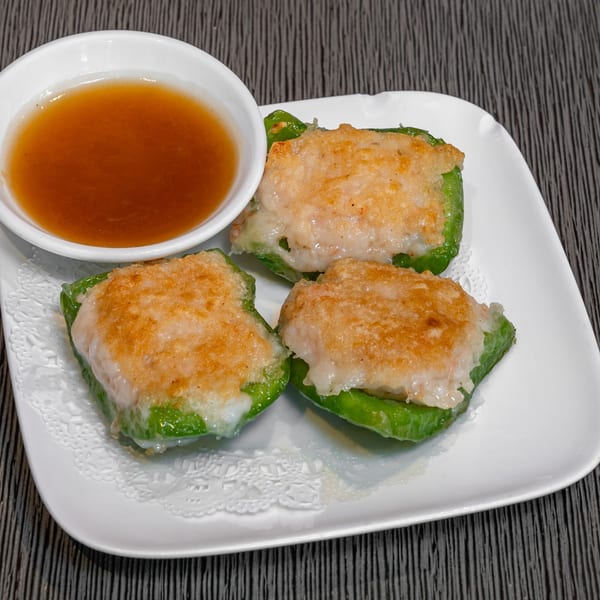 Three green bell peppers stuffed with golden-brown filling, served with a side of dipping sauce.