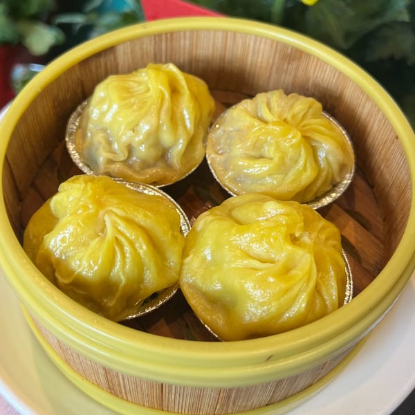 Four yellow dumplings in silver foil cups, served in a bamboo steamer basket.