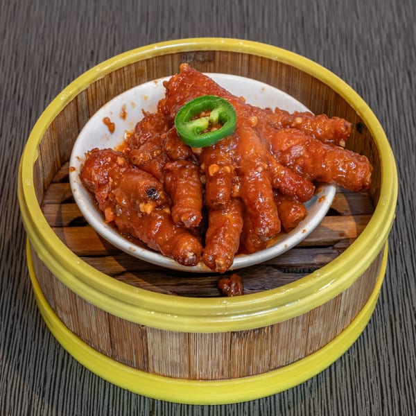 Braised chicken feet in a rich red sauce, garnished with a green chili slice, served in a bamboo steamer.