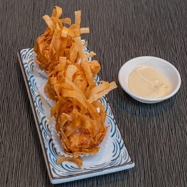 Two crispy fried wonton balls with a side of creamy dipping sauce on a patterned rectangular plate.