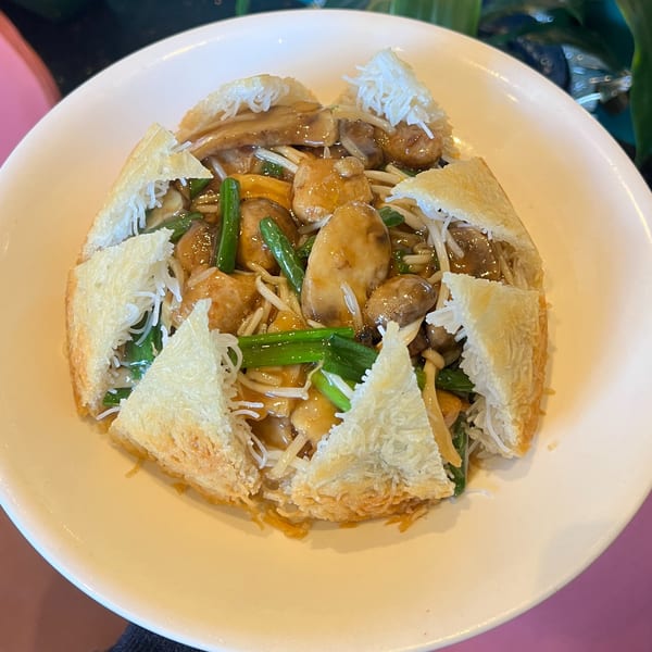 A white bowl filled with stir-fried mushrooms, green beans, and bean sprouts, topped with crispy fried noodles.
