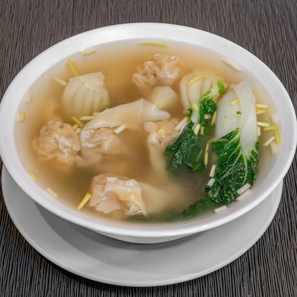 A bowl of Imperial Garden wonton soup with bok choy and scallions on a dark table.