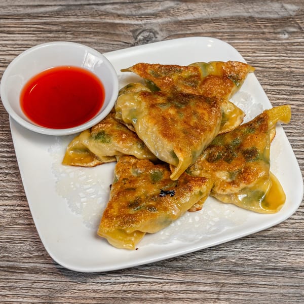 A plate of golden-brown fried dumplings with a side of red dipping sauce on a wooden table.
