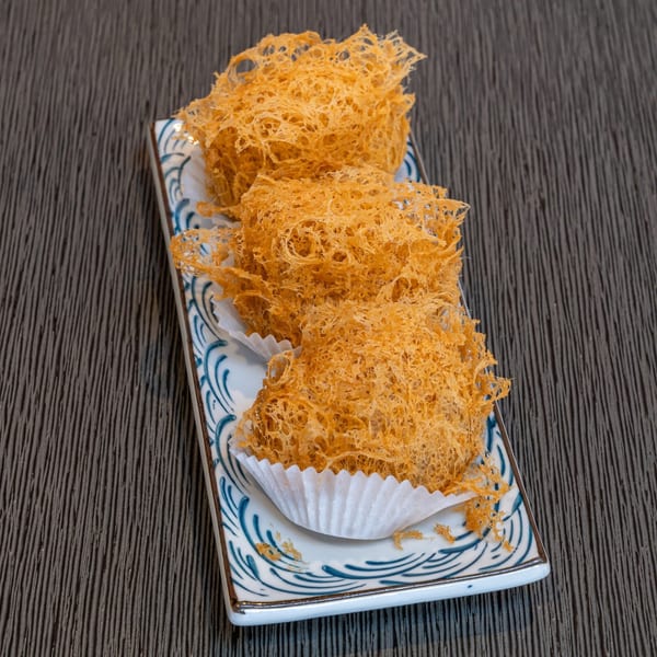 Three crispy fried taro puffs, a Chinese dim sum dish, on a decorative white and blue plate.