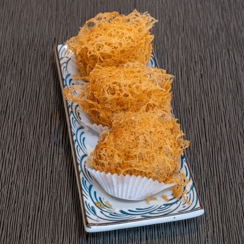 Three crispy fried taro puffs, a Chinese dim sum dish, on a decorative white and blue plate.